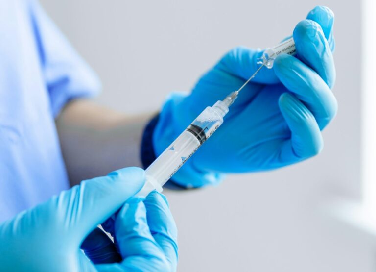 two hands in blue latex gloves fill a syringe with a vaccine